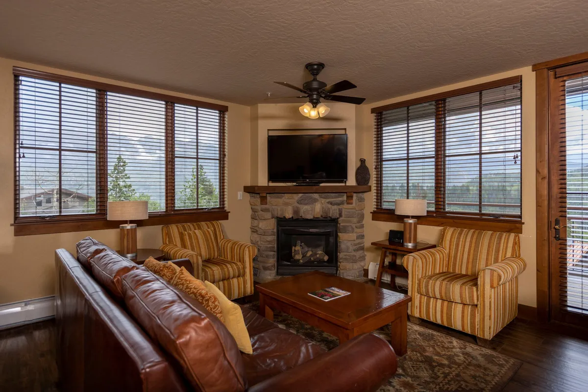 A warmly lit living room with a feature fireplace, comfortable sofa, striped chairs, and a coffee table. The space exudes coziness and is perfect for relaxing, socializing, or unwinding after a day of mountain adventures.